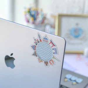 May include: A silver laptop with a sticker of a white sphere with a grid pattern surrounded by various colorful landmarks. The sticker is on the left side of the laptop.