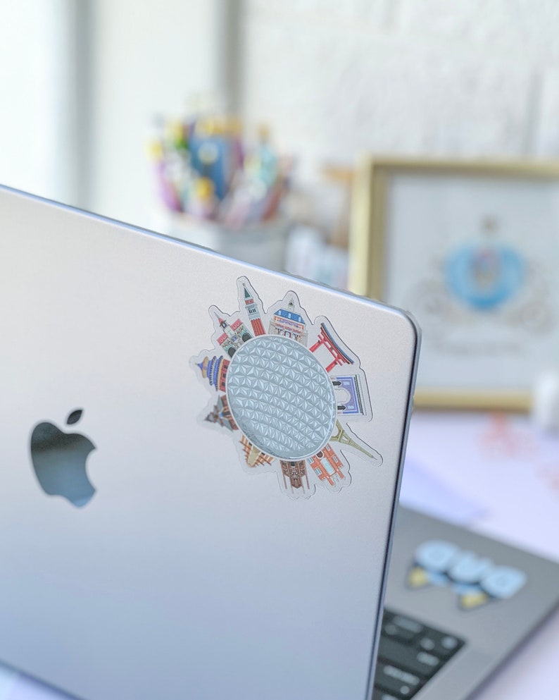 May include: A silver laptop with a sticker of a white sphere with a grid pattern surrounded by various colorful landmarks. The sticker is on the left side of the laptop.