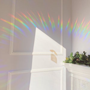 May include: A white wall with white trim and a rainbow prism light reflection. The light is casting a rainbow pattern on the wall.