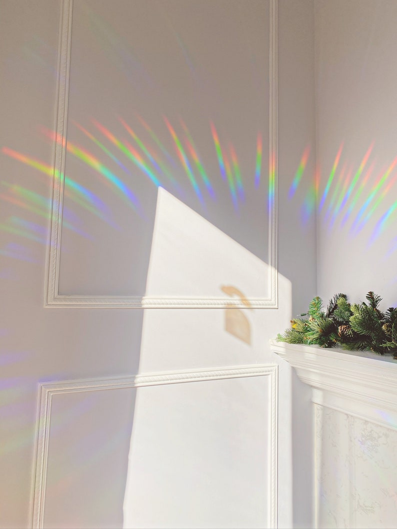 May include: A white wall with white trim and a rainbow prism light reflection. The light is casting a rainbow pattern on the wall.