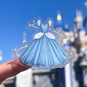 May include: A blue Cinderella ball gown with white puffed sleeves and a white trim around the neckline. The gown is surrounded by gold glitter stars.