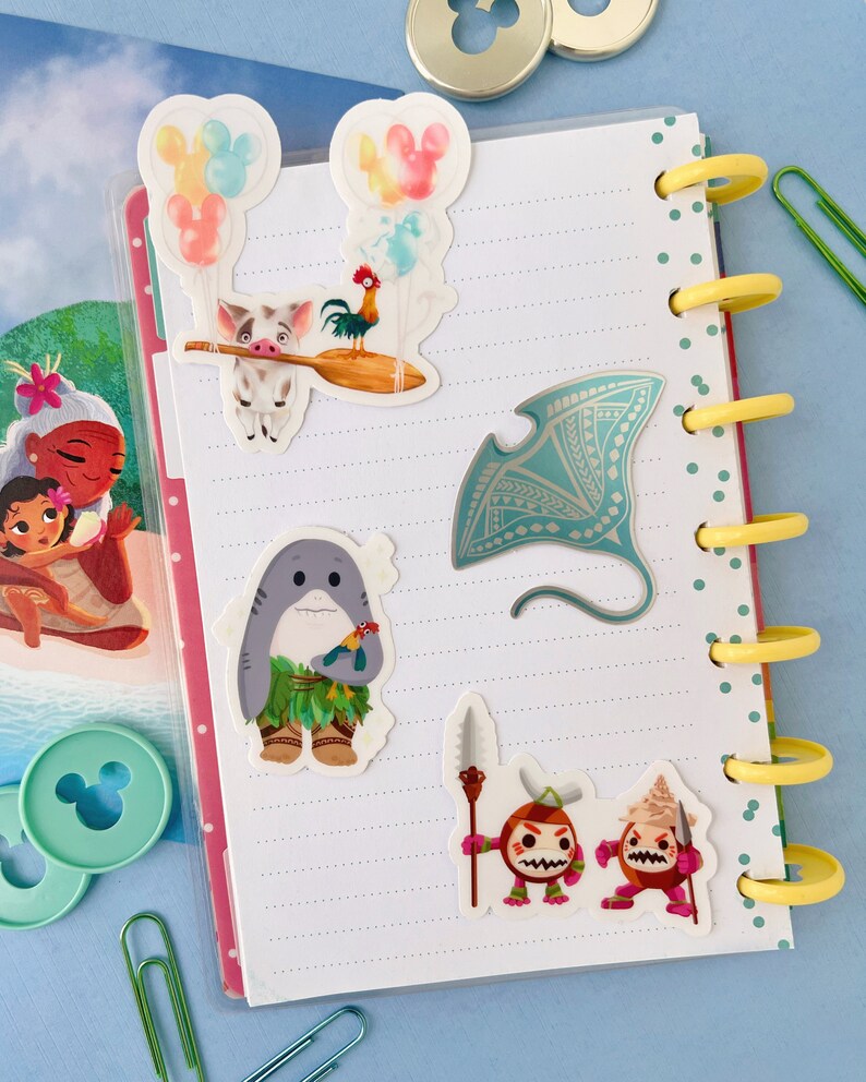 Pu&ograve; includere: Un set di cinque adesivi colorati con personaggi del film Disney Moana. Gli adesivi includono un maiale con un gallo sulla schiena, uno squalo con una collana di fiori, una manta e due piccoli personaggi con lance.