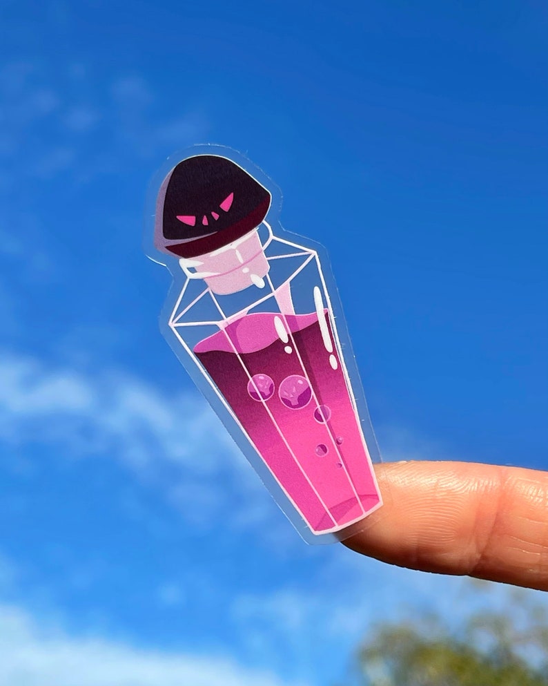 K&ouml;nnte beinhalten: Ein klarer Aufkleber mit einer Cartoon-Trankflasche mit schwarzem Deckel und rosa Fl&uuml;ssigkeit. Die Flasche hat ein geometrisches Design und ist mit rosa Fl&uuml;ssigkeit und Blasen gef&uuml;llt. Der Aufkleber wird vor einem blauen Himmel gehalten.