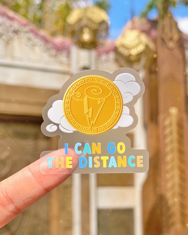 Puede incluir: Adhesivo transparente con una moneda dorada con un rayo y el texto "I CAN GO THE DISTANCE" en letras coloridas. El dise&ntilde;o incluye nubes blancas.
