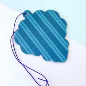 May include: A blue and white striped paper car air freshener with a scalloped edge and a purple string for hanging.
