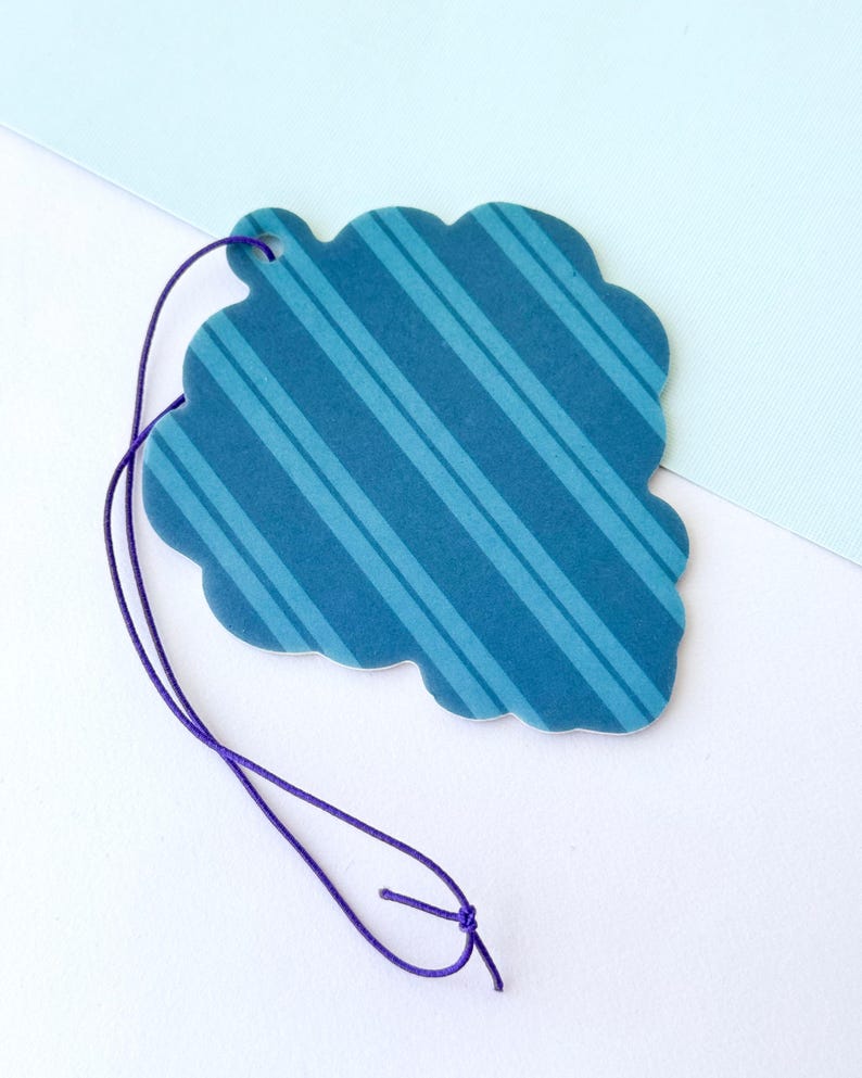 May include: A blue and white striped paper car air freshener with a scalloped edge and a purple string for hanging.