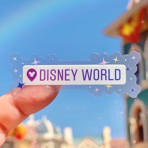 May include: A clear sticker with a purple heart and the text "DISNEY WORLD" in white letters. The sticker has a white border and a cloudy background with colorful stars.