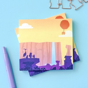 May include: A square sticky note featuring a colorful illustration of a landscape with a waterfall, a tall bird, and a small house floating with a red balloon. The scene includes purple rocky cliffs, a yellow sky, and white clouds.