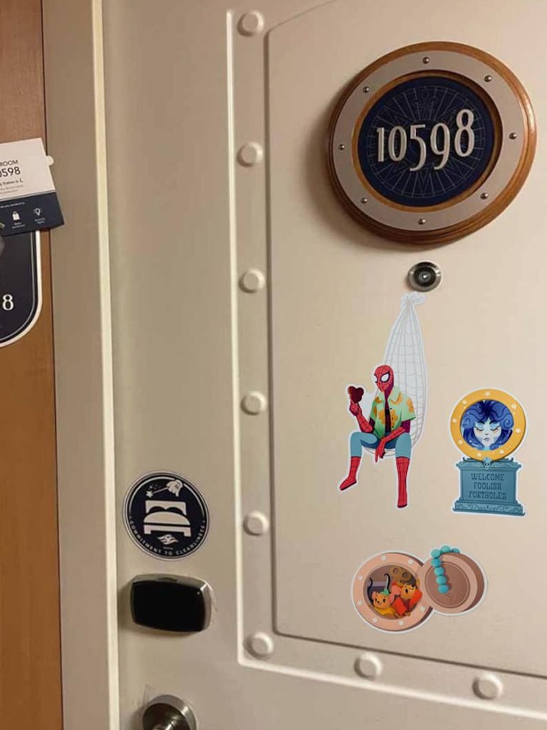 May include: A cream-colored door features a circular room number plaque with the number 10598. Decorative stickers include a Spider-Man figure, a welcome sign, and a nautical-themed design. A door handle and a sign are also visible.