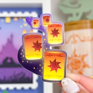 May include: A sticker featuring a cluster of glowing lanterns with a sun design. The lanterns are orange, yellow, and red with a purple background.