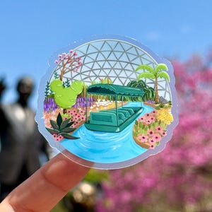 Puede incluir: Un paseo en bote verde y blanco a través de un jardín botánico con un gran domo geodésico en el fondo. El bote está rodeado de flores coloridas y vegetación.