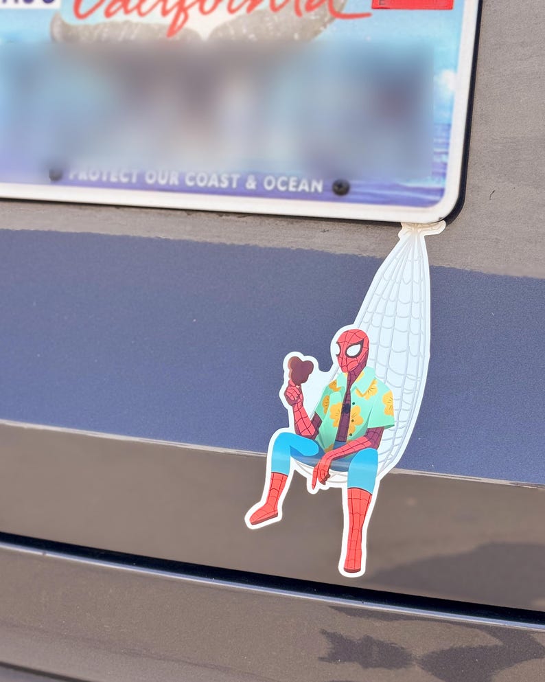 May include: A colorful sticker featuring Spider-Man relaxing in a hammock, holding a chocolate ice cream bar. He wears a Hawaiian shirt, blue pants, and red boots. The sticker is attached to a car near a license plate.