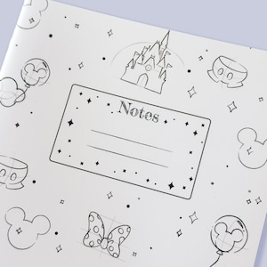 May include: A white notebook cover featuring black line art illustrations of a castle, a polka-dot bow, balloons, and mouse-ear silhouettes. A central rectangular box contains the word Notes with two horizontal lines for writing text.