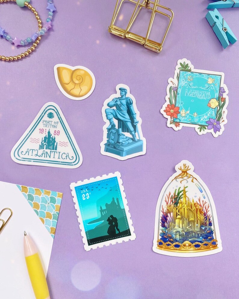 May include: A set of six stickers featuring characters and imagery from the Disney film The Little Mermaid. The stickers are printed on white paper with a glossy finish. The stickers include a seashell, a statue of Prince Eric, a stamp with Ariel and Eric, a book with the title "The Little Mermaid", a sign that reads "Port of Triton 1989 Atlantica", and a dome-shaped sticker with a depiction of Ariel's castle.