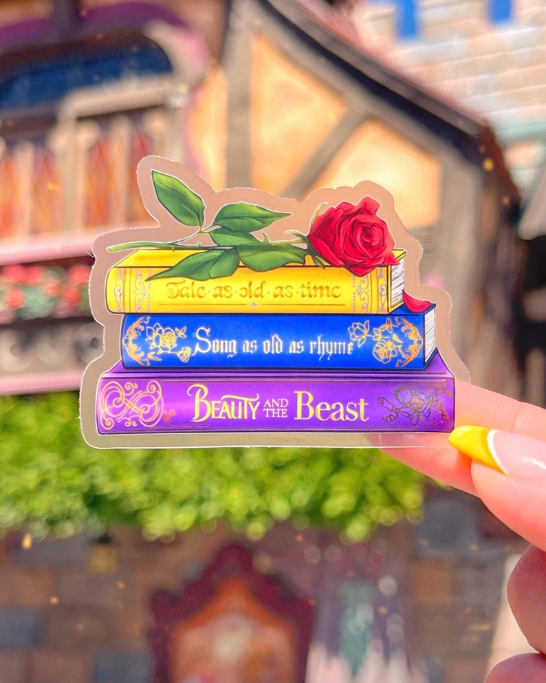 May include: A clear sticker featuring a stack of three books. The top book is yellow with the text "Tale as old as time". The middle book is blue with the text "Song as old as rhyme". The bottom book is purple with the text "Beauty and the Beast". A red rose with green leaves sits on top of the books.