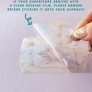 May include: A clear protective film is being peeled off a suncatcher with a sun and stars design. The text "IF YOUR SUNCATCHER ARRIVES WITH A CLEAR BACKING FILM, PLEASE REMOVE BEFORE STICKING IT ONTO YOUR WINDOWS!" is visible in the image.