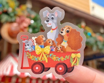 May include: A clear sticker featuring a red wagon filled with cartoon puppies and two adult dogs. The wagon has a yellow bow and is decorated with green leaves and berries. The dogs are in various colors, including gray, brown, and tan.