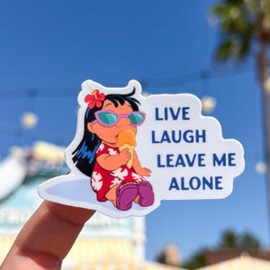 May include: A sticker featuring a cartoon character with black hair, sunglasses, and a red dress, holding an ice cream cone. The sticker has the text "LIVE LAUGH LEAVE ME ALONE" in blue letters on a white cloud-shaped background.