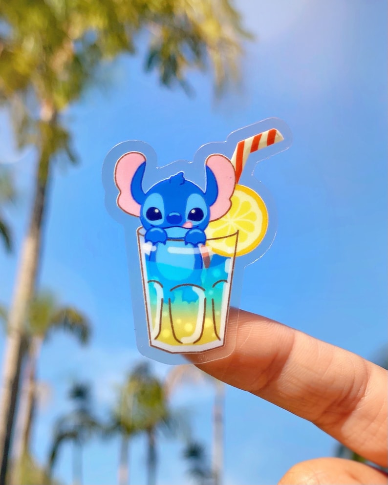 Puede incluir: Un personaje de dibujos animados azul con orejas grandes est&aacute; dentro de un vaso de limonada con una rodaja de lim&oacute;n y una pajita roja y blanca a rayas. El personaje sonr&iacute;e y tiene la lengua azul que sobresale. El vaso est&aacute; en un dedo.