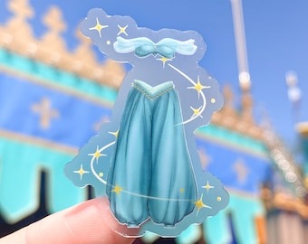 May include: A clear sticker with a blue and gold illustration of a genie costume. The costume includes a blue top and pants with gold accents. The sticker is surrounded by a white background with gold stars.