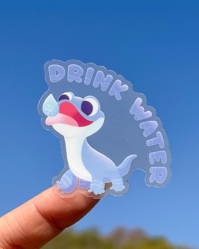 May include: A clear sticker featuring a blue cartoon lizard drinking water. The sticker reads "Drink Water" in a purple font.