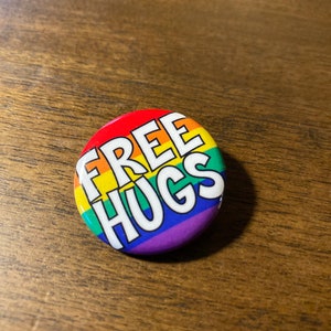 May include: A round button with a rainbow design and the text "FREE HUGS" in white.