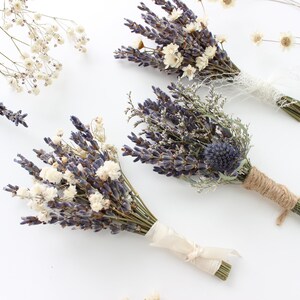 May include: Three bouquets of dried lavender and white flowers tied with twine and ribbon. The bouquets are arranged on a white surface.