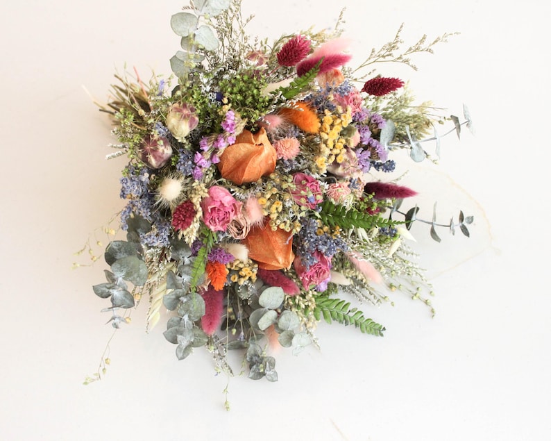 May include: A vibrant bouquet of dried flowers featuring a mix of colors including pink, orange, purple, and green. The arrangement includes various textures and shapes, with eucalyptus leaves and seed pods.