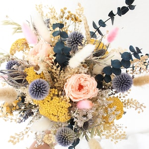 May include: A dried flower bouquet with a mix of yellow, pink, white, and blue flowers. The bouquet includes dried roses, eucalyptus, and other dried flowers.