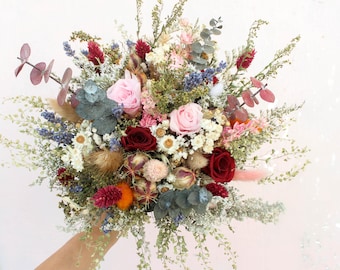 Könnte beinhalten: Ein lebendiger Strauß aus Trockenblumen mit rosa Rosen, burgunderfarbenen Blüten und verschiedenen Grünpflanzen. Das Arrangement umfasst blaue, weiße und orangefarbene Akzente und schafft eine farbenfrohe und strukturierte Darstellung. Ein schönes Blumenarrangement.