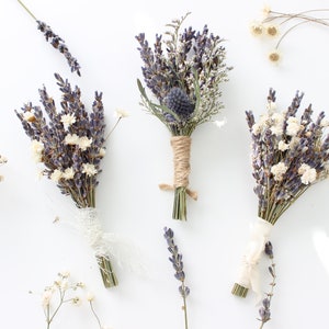 May include: Three small bouquets of dried lavender and white flowers tied with twine and ribbon. The bouquets are arranged on a white background.