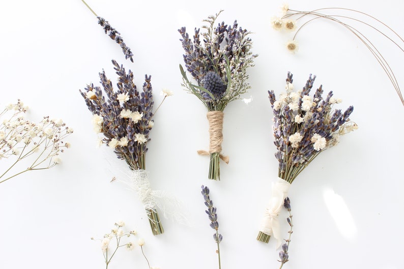 May include: Three small bouquets of dried lavender and white flowers tied with twine and ribbon. The bouquets are arranged on a white background.