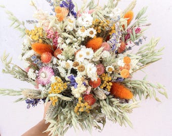 Puede incluir: Un ramo de flores secas con una mezcla de flores blancas, naranjas, amarillas, rosas y moradas. El ramo está atado con una cuerda natural e incluye hierbas y trigo secos.