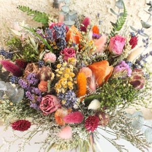 May include: A vibrant bouquet of dried flowers featuring a mix of colors including pink, orange, yellow, and purple. The arrangement includes roses, lavender, and various types of foliage. The bouquet is tied together, creating a natural and rustic aesthetic.