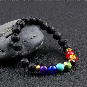 Peut inclure: Un bracelet en perles de roche volcanique noire avec sept perles de pierres précieuses colorées. Les perles sont rouges, orange, jaunes, vertes, turquoise, bleues et violettes.