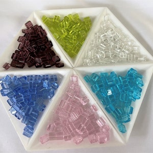 Peut inclure: Six petits plats triangulaires remplis de perles de verre de différentes couleurs. Les perles sont dans des tons de violet, vert, clair, bleu, rose et turquoise.