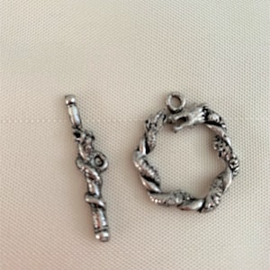 Può includere: Set di chiusura a levetta color argento. La chiusura presenta una barra con un design a spirale e un anello circolare con un dettaglio a testa di drago. La chiusura è progettata per la creazione di gioielli e l'artigianato.