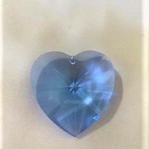 May include: A light blue crystal heart pendant with a faceted design. The heart is approximately 2 inches in length and width.