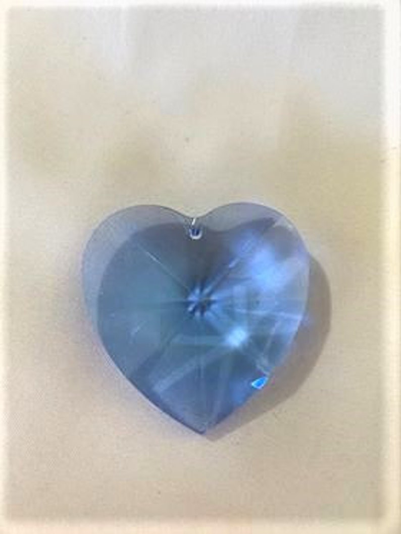 May include: A light blue crystal heart pendant with a faceted design. The heart is approximately 2 inches in length and width.