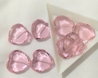 May include: Eight pink glass heart-shaped beads. The beads are faceted and have a hole through the center for stringing.