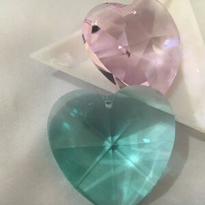 May include: Two heart-shaped crystal prisms, one pink and one teal, on a white surface.