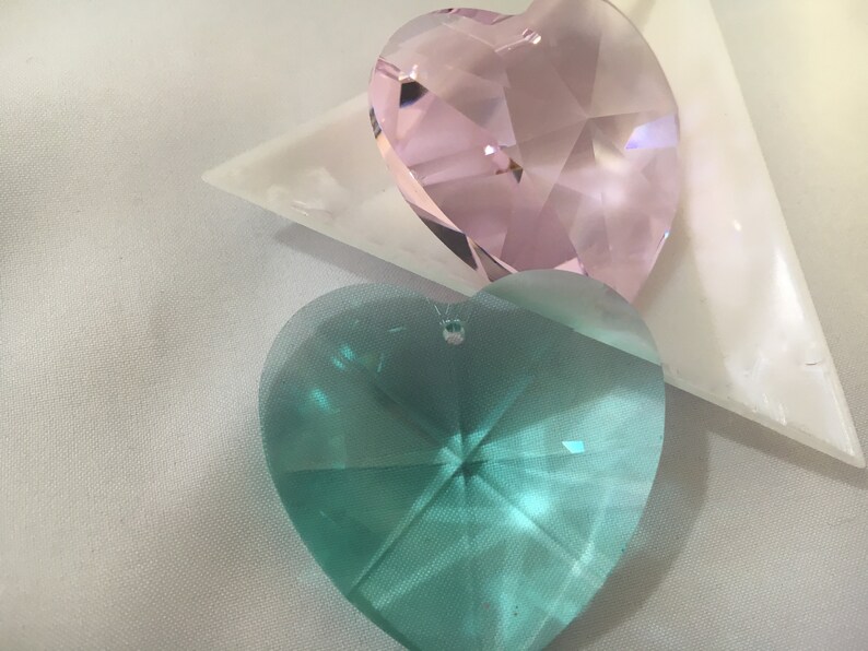 May include: Two heart-shaped crystal prisms, one pink and one teal, on a white surface.