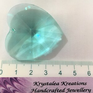 May include: A light blue crystal heart charm with a faceted design. The charm is approximately 2 inches in length and is shown next to a ruler for size reference.