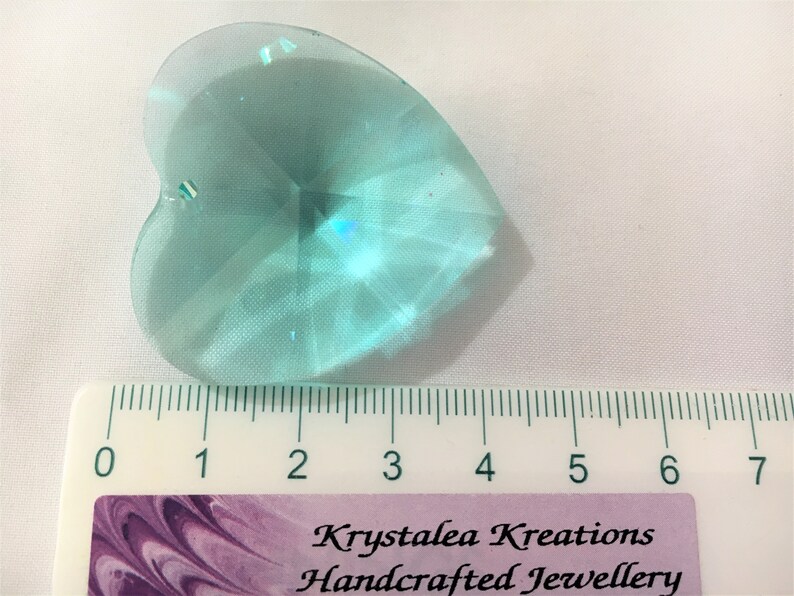 May include: A light blue crystal heart charm with a faceted design. The charm is approximately 2 inches in length and is shown next to a ruler for size reference.