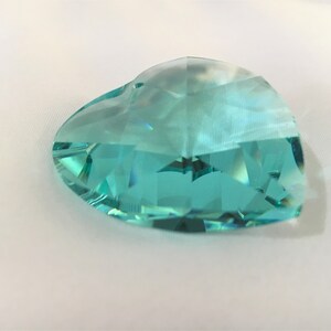 May include: A large, faceted, teal blue crystal heart. The crystal is clear and has a slight iridescent sheen.