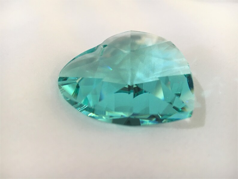 May include: A large, faceted, teal blue crystal heart. The crystal is clear and has a slight iridescent sheen.