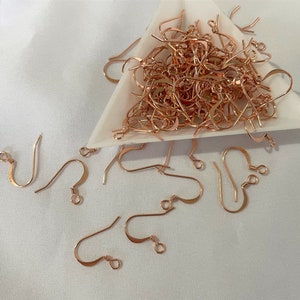 Peut inclure: Un tas de crochets d'oreille en or rose dans un plat triangulaire blanc. Les crochets sont éparpillés sur une surface blanche.