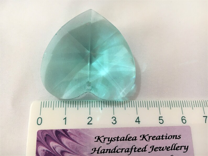 May include: A light blue heart-shaped crystal prism measuring approximately 2 inches in length. The prism is faceted and has a clear, glassy appearance.