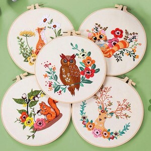 Peut inclure: Cinq cerceaux à broder avec des motifs différents. Les motifs comprennent un renard, un hibou, un chat, un cerf et un écureuil. Chaque motif est entouré de fleurs.