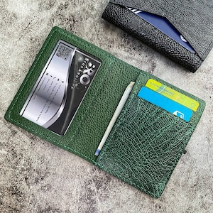 May include: A green leather wallet with a card slot and a clear window for a business card. The wallet has a textured surface and is stitched with white thread. The text "BRO Bros Leather" is visible on the business card.